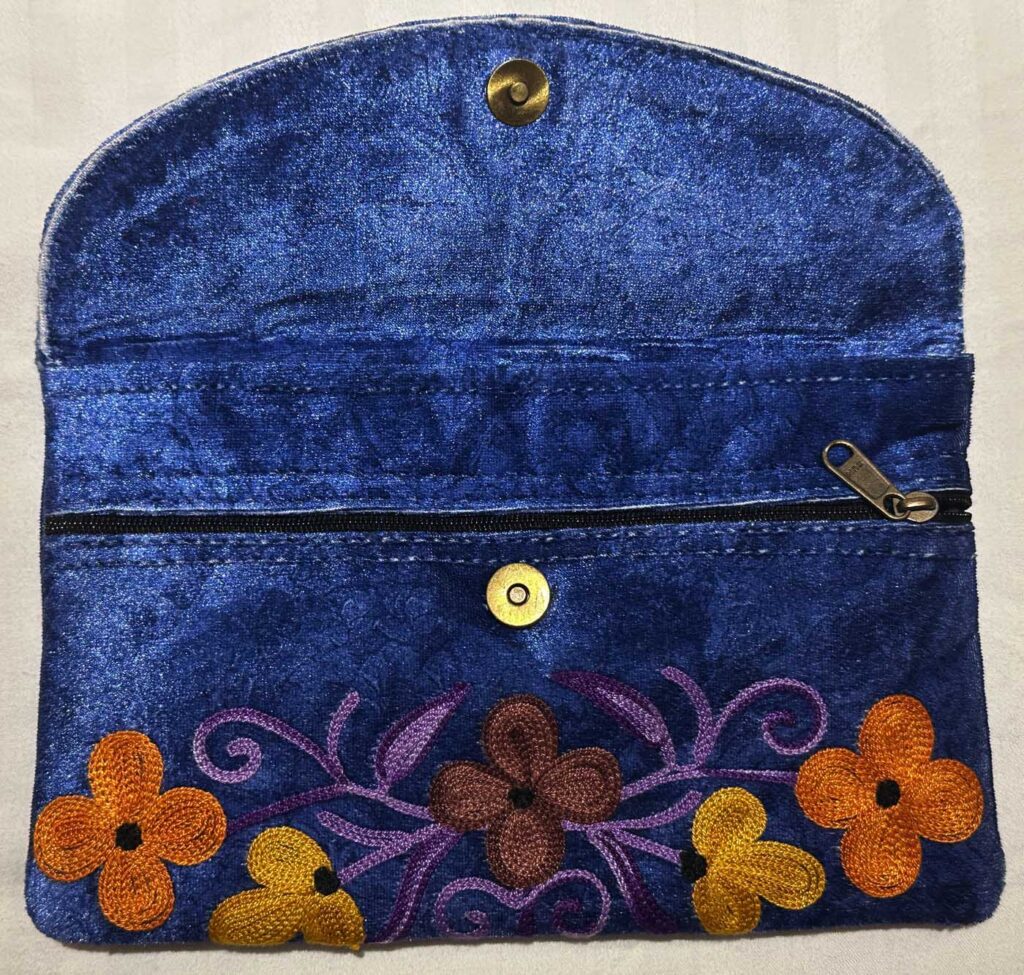 The navy clutch with its flap opened out, plain navy interior, brass magnetic snaps and a zipped inner pocket