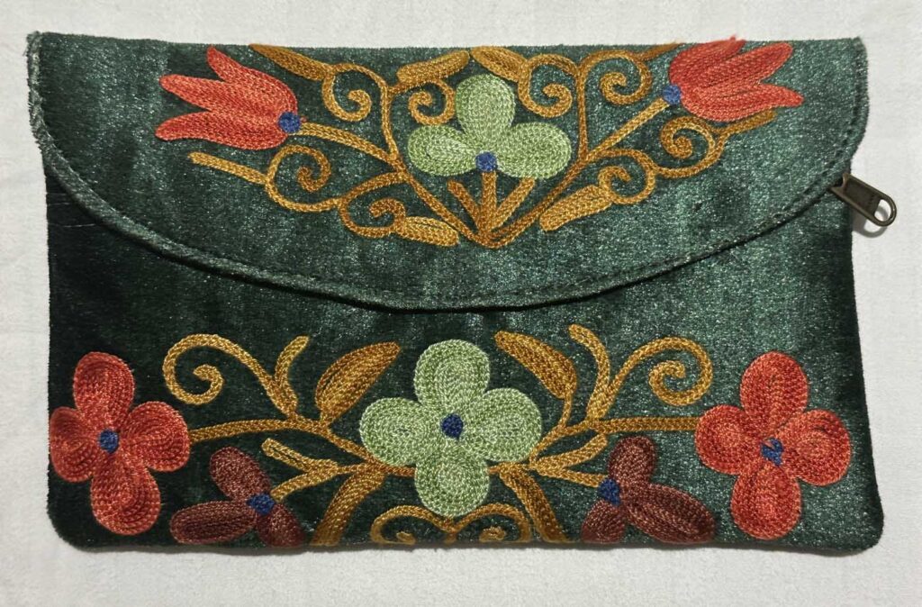 Flat front view of the sage-green clutch on a pale ground, the full embroidered pattern of leaves, trefoils and coral flower centres