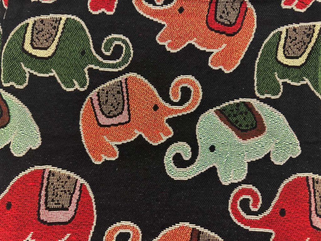 Close view of the black fabric, the cream-outlined elephants in olive, terracotta, mint and red standing out against the dark weave