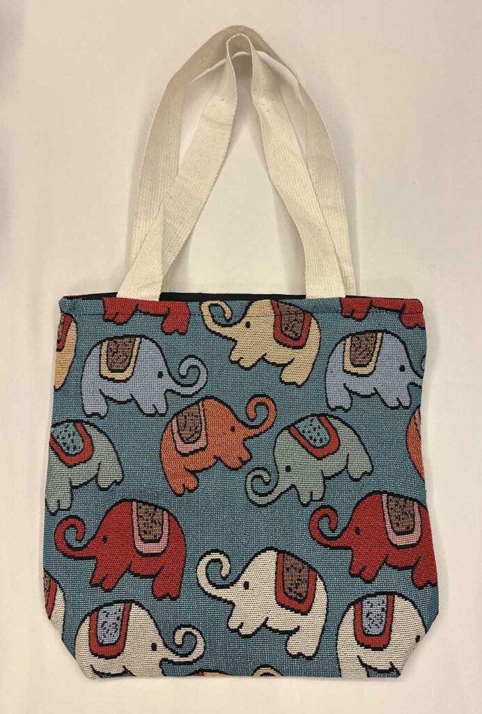 The teal-blue elephant tote laid flat with handles extended, the black top binding just visible under the woven edge