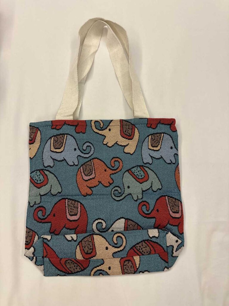 The teal-blue tote front-on, handles folded, showing the horizontal fold where the bag creases above the base