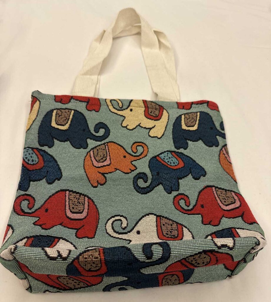 The sage-green tote photographed slightly from above so the gusseted base and the pattern wrapping around it are both visible
