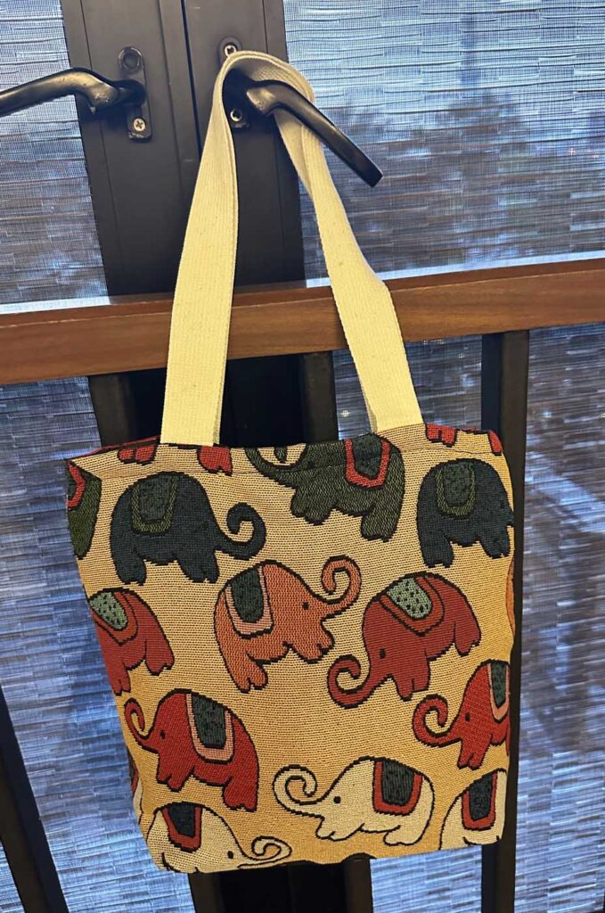 The cream-yellow tote hung from a black door handle, its long strap taut, the woven elephants in charcoal, terracotta and orange clearly visible