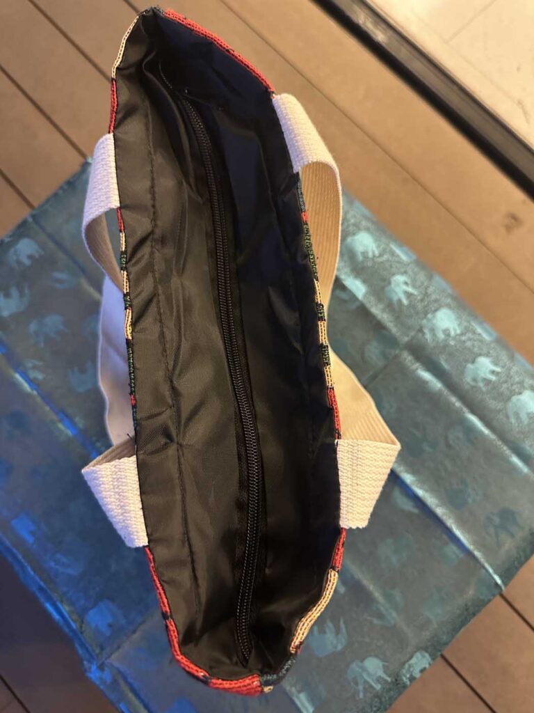 The bag opened from above at an angle, showing the black nylon lining, the full-length top zip and the woven multicolour binding along the opening