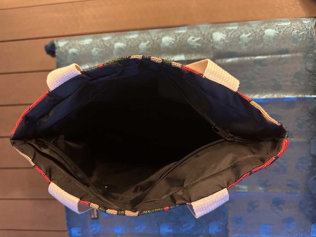 Looking straight down into the open bag: black lining, a zipped interior pocket across the back wall, and the cream handles falling to either side