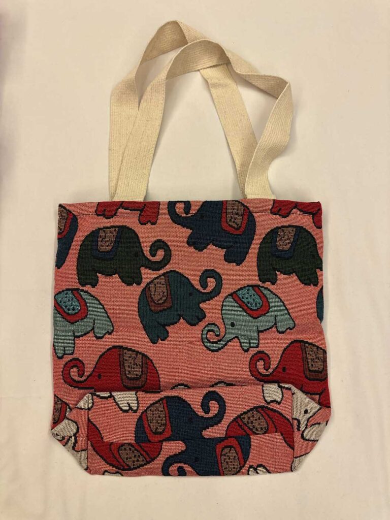 The salmon-pink elephant tote laid flat with its handles extended upward, showing the full front panel and the fold across the base
