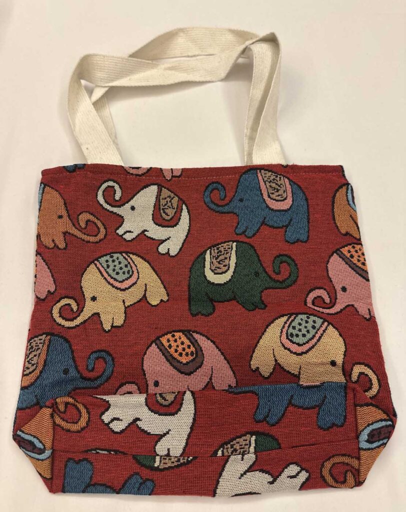 The red elephant tote seen front-on with its long cream shoulder strap doubled over the top edge