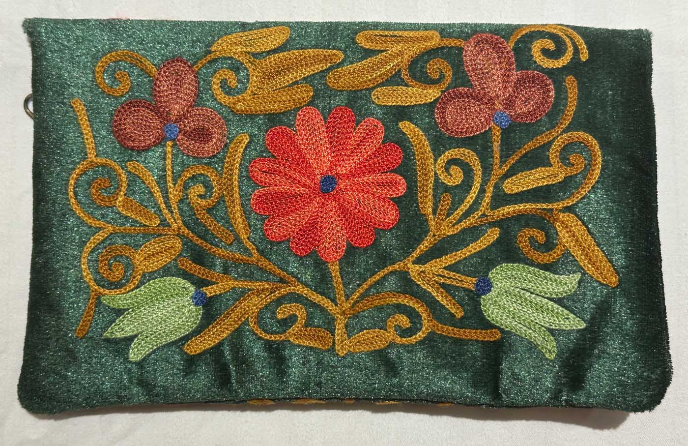 A dark green suede clutch bag embroidered in gold chain stitch with scrolling vines, a large coral flower at the centre, dusky pink blossoms and pale green buds