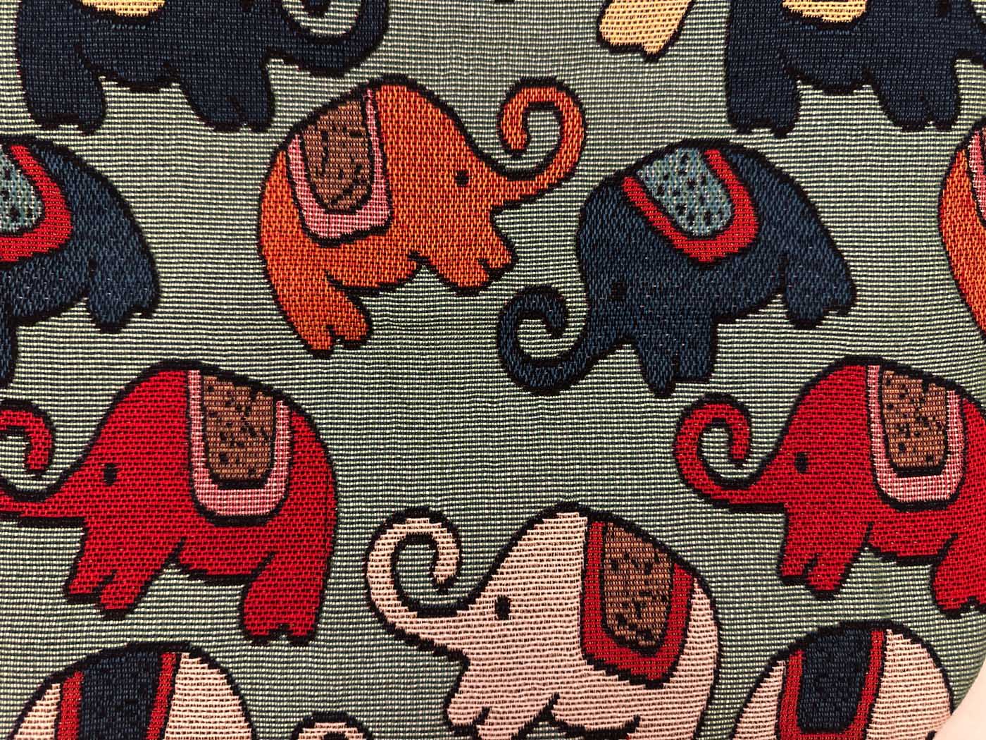 Close view of sage-green woven fabric patterned with elephants in red, navy, orange and blush, each carrying a small woven saddle blanket