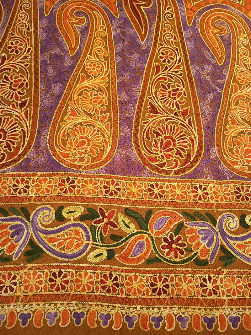 Orange and gold paisleys embroidered on a purple ground above the brown stole's daisy-chain borders and its fringe of purple and orange petals
