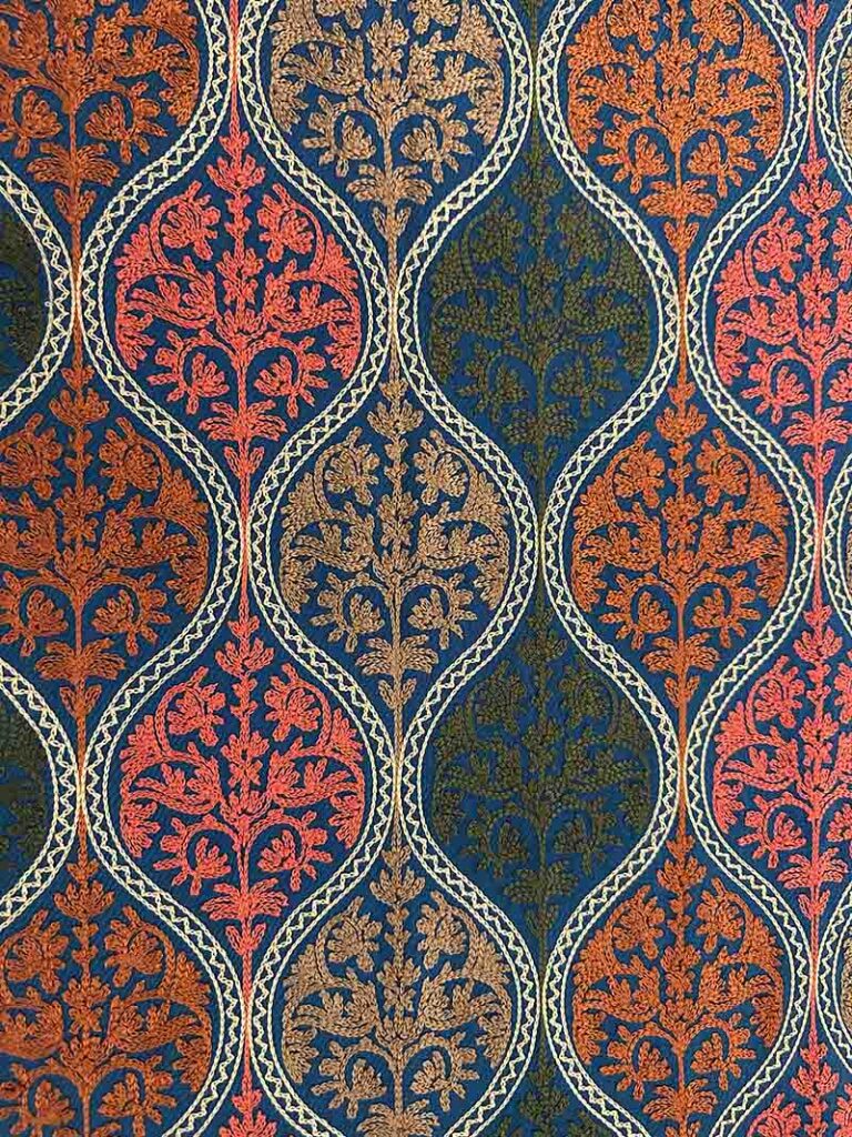 Close view of the petroleum-blue stole's medallion field: teardrop shapes outlined in cream chain stitch, each filled with a flowering spray in coral, orange, olive or tan