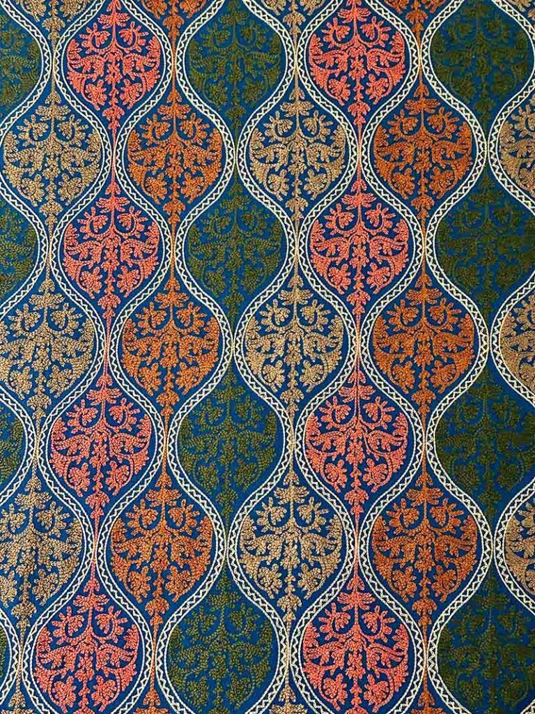 The densest part of the petroleum-blue embroidery, medallions in coral, orange, gold and olive packed edge to edge with no plain wool showing