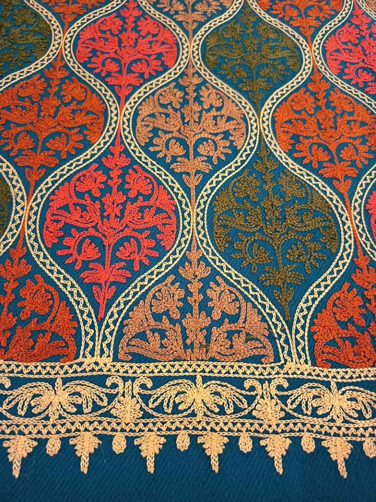 The medallion field meeting the gold border: coral, olive and tan sprays above a braided band and a row of scalloped gold picots on plain blue