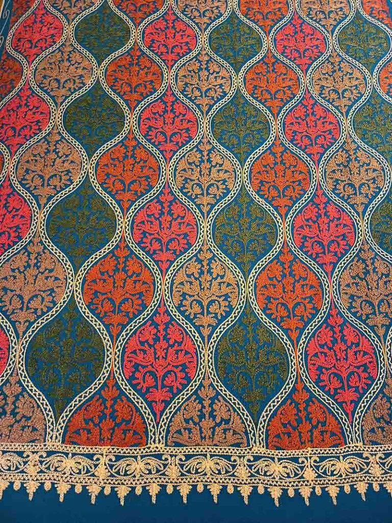 A tall view of the petroleum-blue panel: five rows of embroidered medallions closing on the gold border and its picot edge at the bottom
