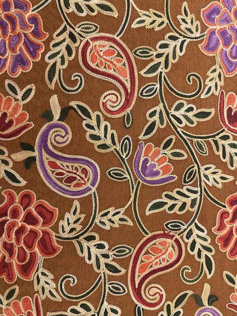 Close view of the brown stole's centre field: a cream vine winding between deep red and purple blossoms, small paisleys and dark green leaves on plain brown wool