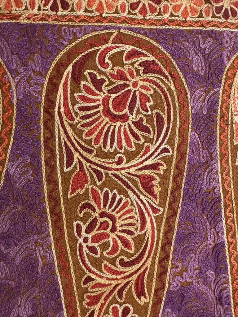 One large paisley filling the frame: brown ground inside a cream outline, filled with red and gold chrysanthemums, set against a densely embroidered purple field