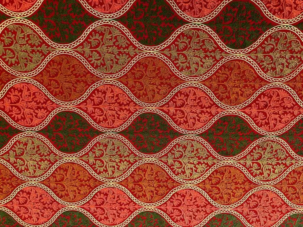 Close view of the crimson stole's field: undulating cream-gold bands separating rows of coral, olive and gold flowering sprays on deep red wool