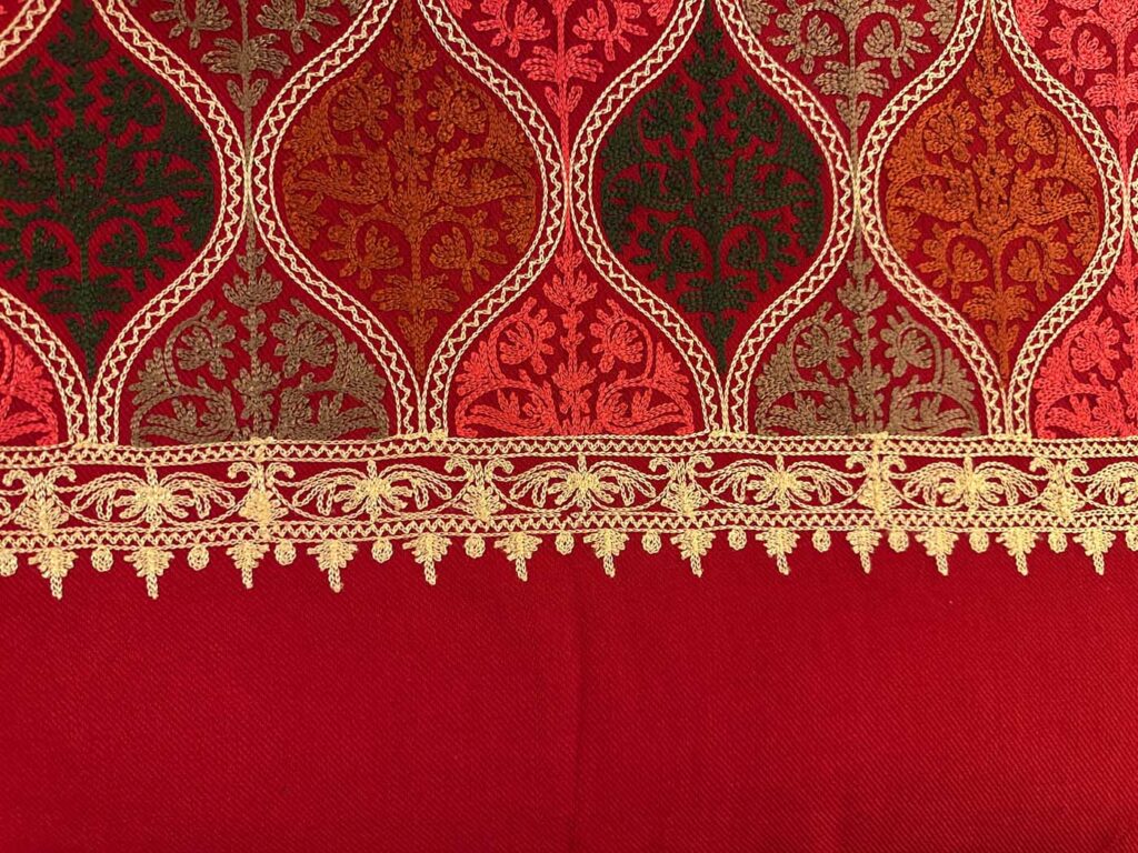 The crimson medallion field ending at a gold border of scrolling flowers and picots, with plain deep-red wool below