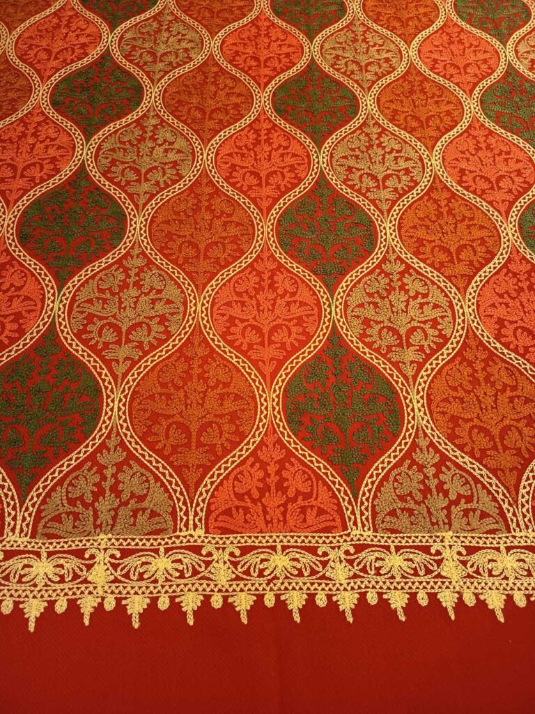 A tall view of the crimson panel: rows of embroidered medallions in orange, olive and gold narrowing to the gold border and its picot fringe