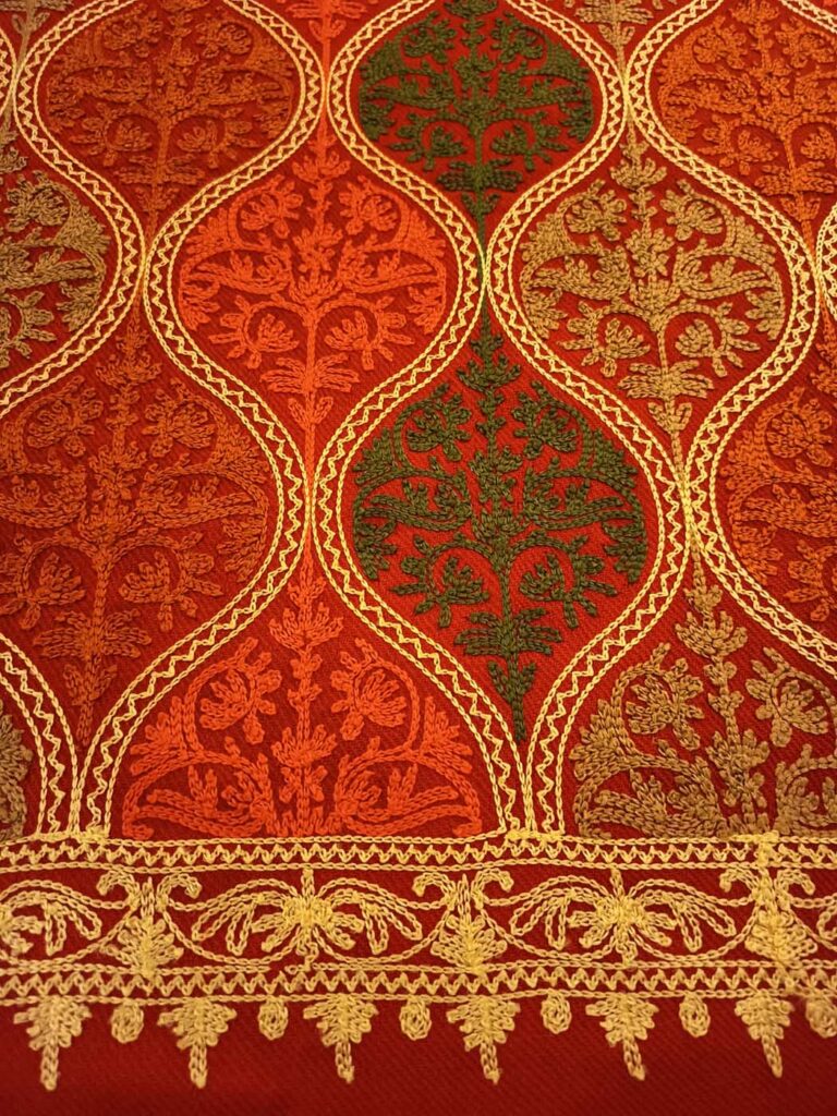 The crimson field at close range in warmer light, deep orange and olive sprays inside gold-outlined medallions above the scrolling gold border